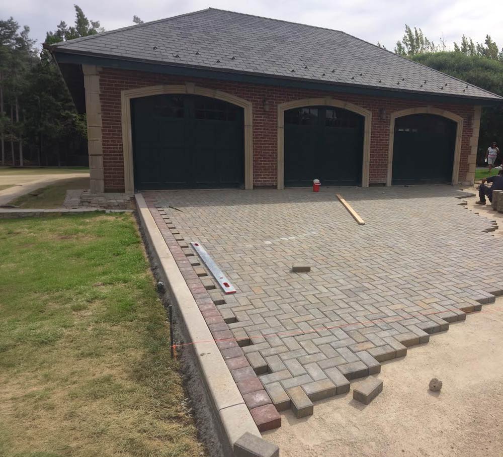 An incomplete paver driveway in front of a three-door garage