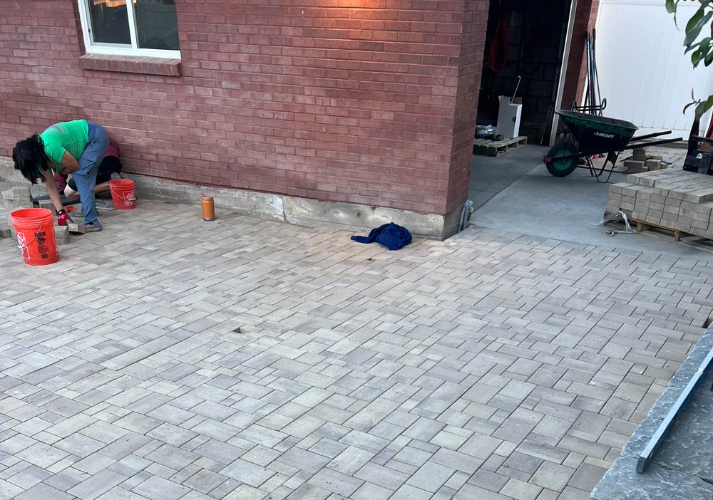 A figure bending down to install pavers outside a red-brick house