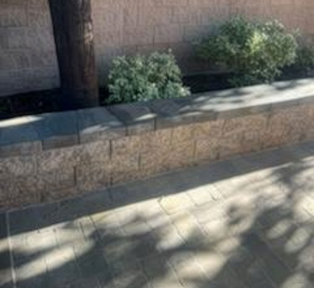 A retaining wall near a taller wall with bushes and trees installed between them