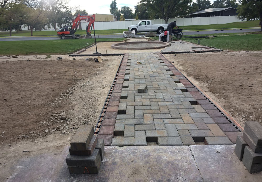 A half-finished walking back made from multiple colors of bricks, running from a porch to the road